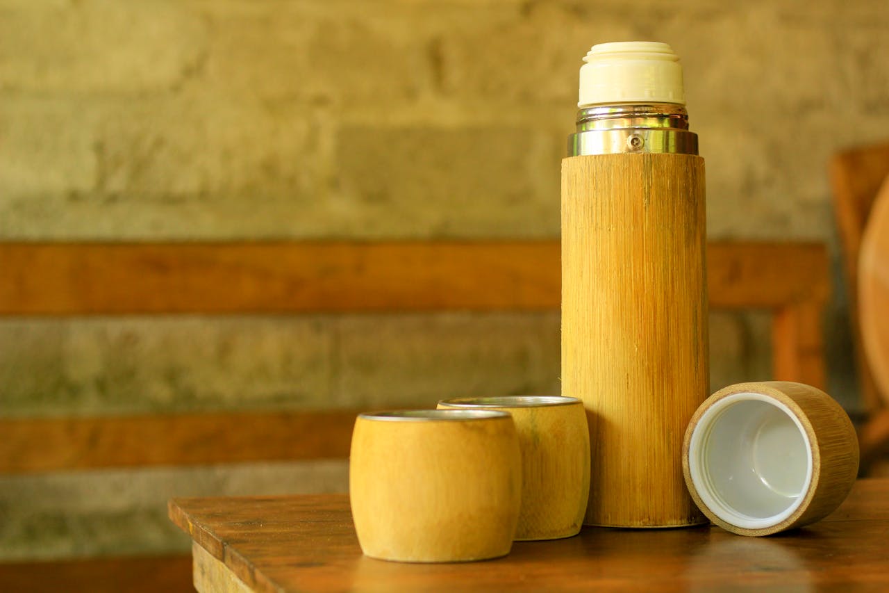 Close-up of a bamboo thermos with matching cups on a wooden table indoors.